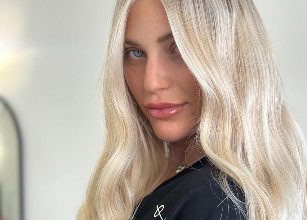 Person with long blonde hair wearing a black top in a neutral setting